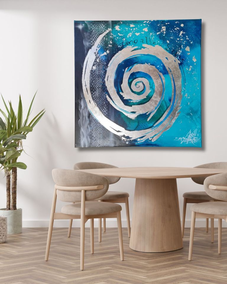 Runder Holztisch mit vier gepolsterten hellbeigen Stühlen in einem Raum mit hellgraßer Wand, an der ein blaues abstraktes Kunstwerk mit silberner Spirale hängt, daneben steht eine Pflanze in einem Topf.